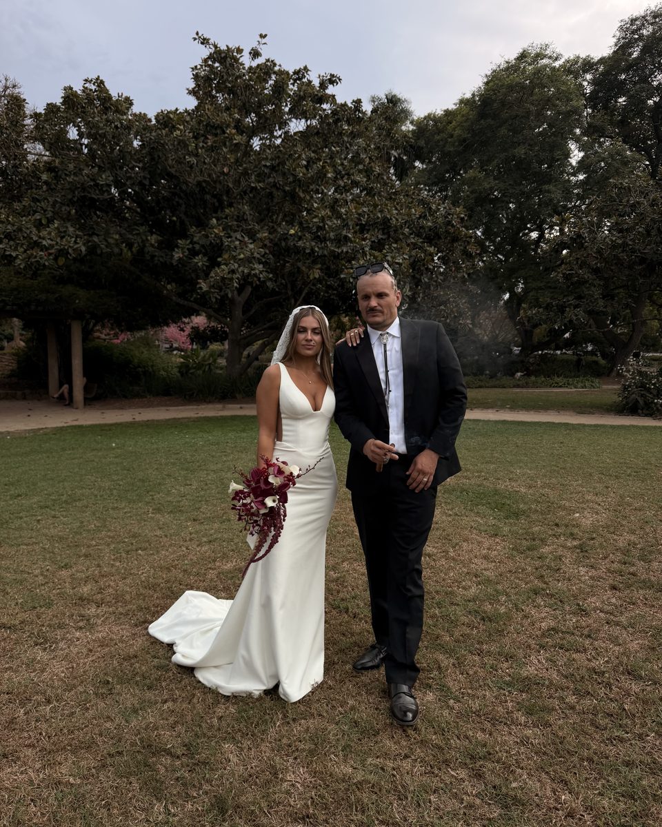 Bride and groom walking across a lawn with her bouquet