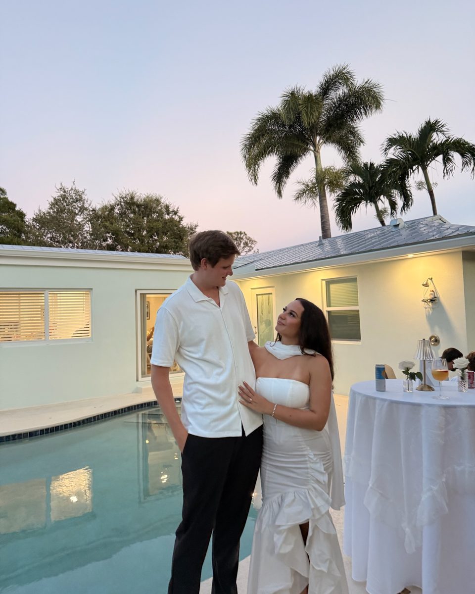 Couple laughing by a pool at dusk under palms